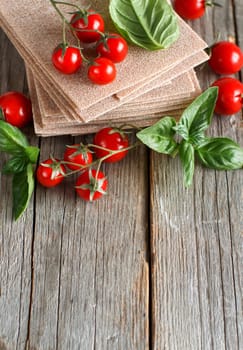 Raw lasagna sheets,basil and cherry tomatoes on a wooden table