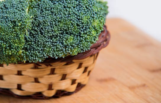close up on fresh broccoli in basket solated on wood and white background