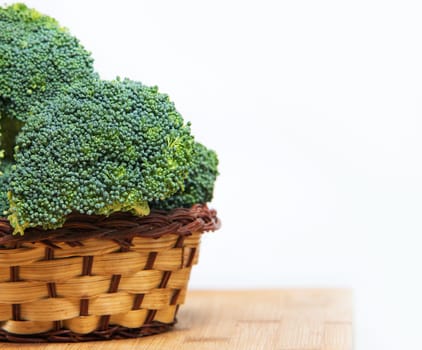 close up on fresh broccoli in basket solated on wood and white background