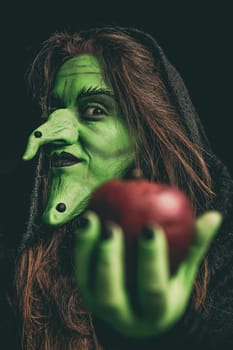Green witch holding an apple in her hand. Shallow depth of field.