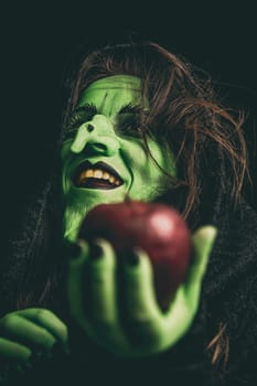 Green witch laughing while holding an apple in her hand. Shallow depth of field.