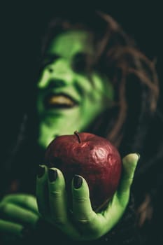 Witch green hand holding a rotten red apple while laughing. Shallow depth of field.