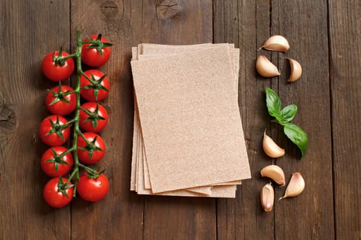 Whole wheat lasagna sheets, tomatoes, garlic and basil on wooden background