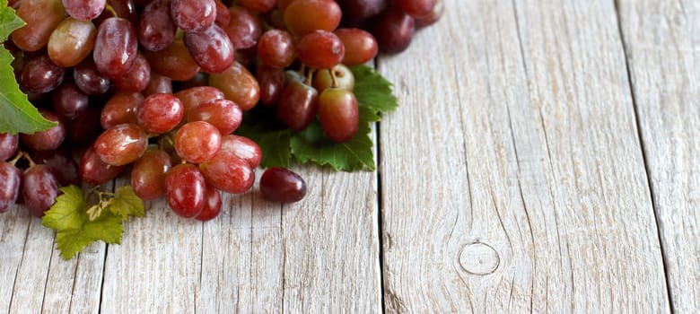 Red grapes with leaves on a old wooden table close up