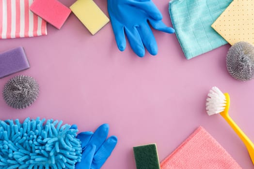 Collection of pastel-coloured cleaning supplies on pink background with copyspace