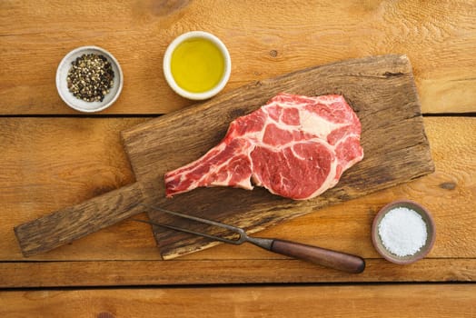 Dry aged Rib eye steak on wooden board with pepper, salt and oil