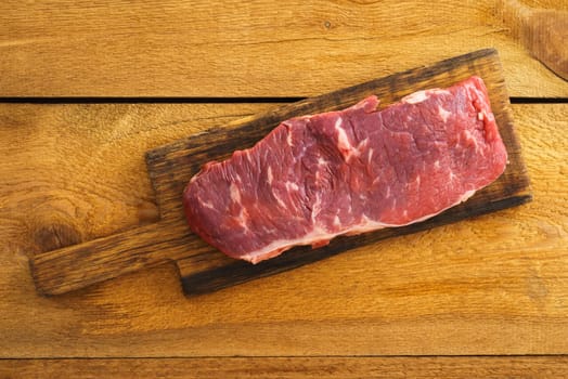 Uncooked rump steak on wooden board on wood
