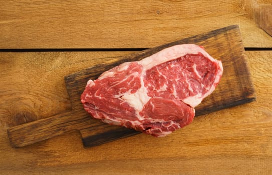 Uncooked rib eye steak on wooden board