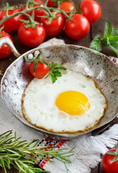 Fried egg with tomatoes and herbs n a old frying pan on wood