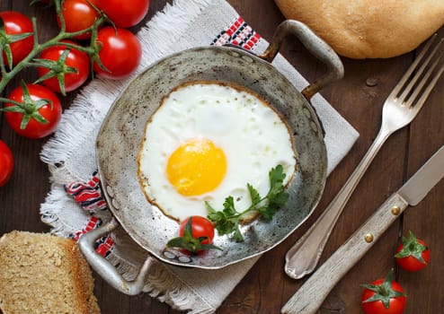 Fried egg with tomatoes, homemade bread and herbs on a old frying pan on wood