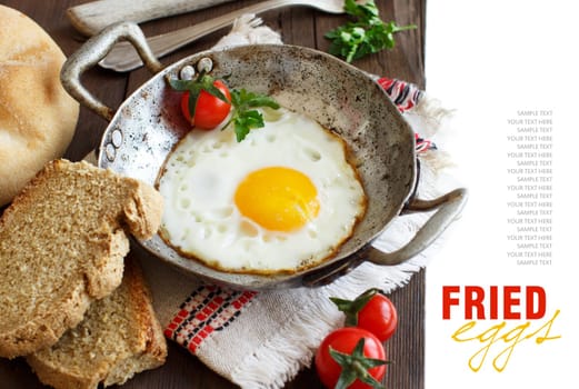 Fried egg with tomatoes, homemade bread and herbs on a old frying pan on wood