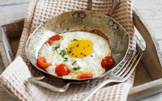 Fried egg with tomatoes and herbs on a old frying pan on wood