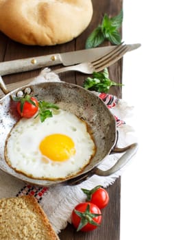 Fried egg with tomatoes, homemade bread and herbs on a old frying pan on wood