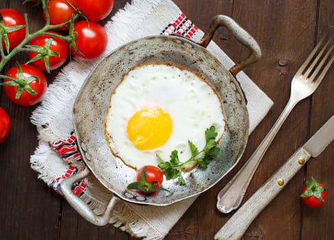 Fried egg with tomatoes and herbs n a old frying pan on wood