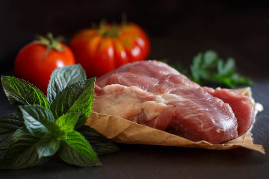 Slice of raw turkey steak with herbs and tomatoes on dark background