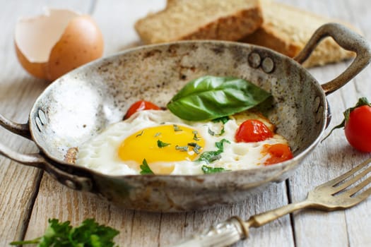Fried egg with tomatoes, homemade bread and herbs on a old frying pan on wood
