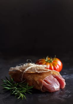 Slice of raw turkey steak with rosemary and tomatoes on dark background
