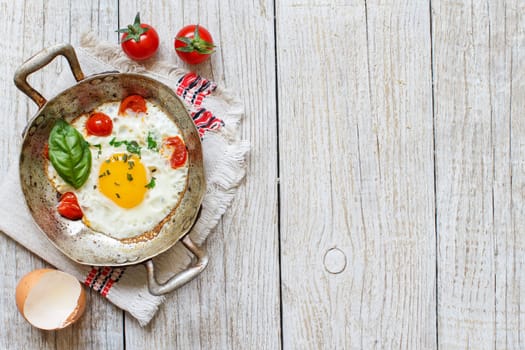 Fried egg with tomatoes and herbs n a old frying pan on wood