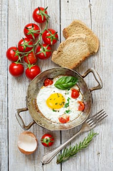 Fried egg with tomatoes, homemade bread and herbs on a old frying pan on wood