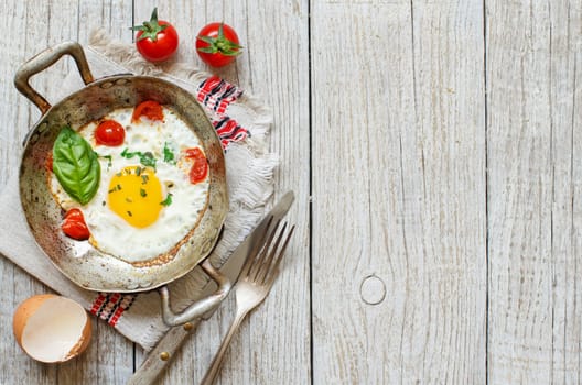 Fried egg with tomatoes and herbs n a old frying pan on wood