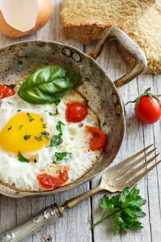 Fried egg with tomatoes, homemade bread and herbs on a old frying pan on wood
