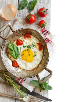 Fried egg with tomatoes and herbs on a old frying pan on wood