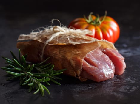 Slice of raw turkey steak with rosemary and tomatoes on dark background