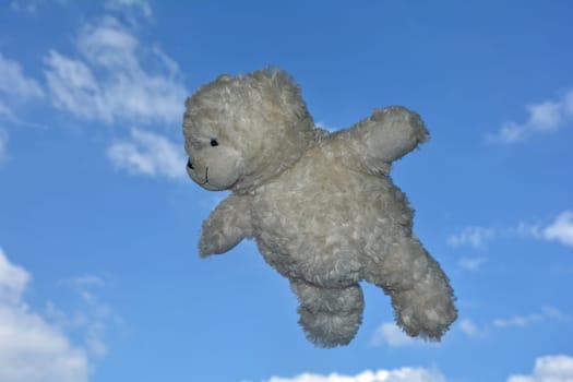 White Teddy Bear flies in the air under blue sky with clouds