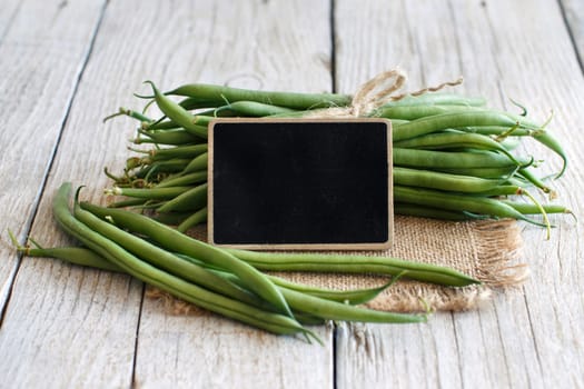 Fresh green french beans with a small chalkboard on a wooden background