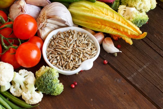 Raw Rye Grain in a bowl and vegetables on wood