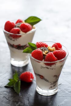 Yogurt with chia seeds, walnuts, mint and raspberries on dark background