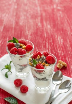 Yogurt with chia seeds, walnuts, mint and raspberries on red background