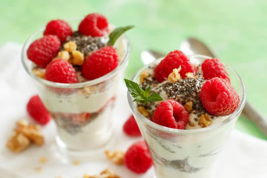 Yogurt with chia seeds, walnuts, mint and raspberries on green background