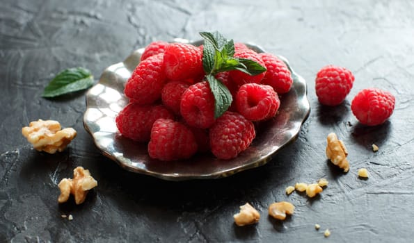Raspberries, walnuts and mint leaves on dark background top view