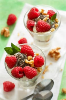 Yogurt with chia seeds, walnuts, mint and raspberries on green background