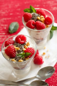 Yogurt with chia seeds, walnuts, mint and raspberries on red background