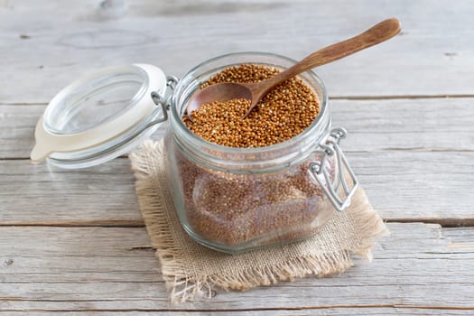 Raw brown millet in a glass jar on wooden background