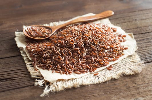 Uncooked Red rice with a wooden spoon close up