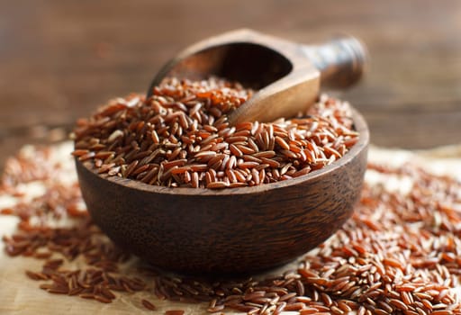 Uncooked Red rice in a bowl with a wooden spoon on the table