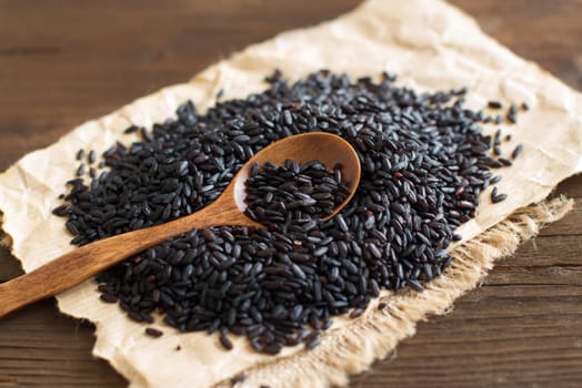 Black rice with a spoon on a wooden table close up