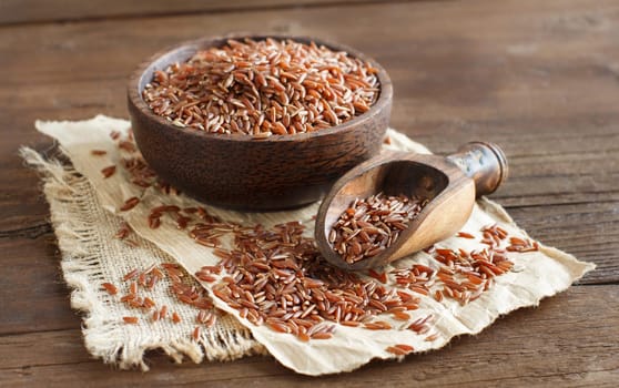 Uncooked Red rice in a bowl with a wooden spoon on the table