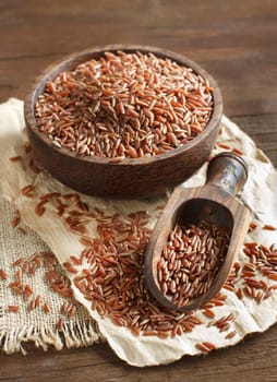 Uncooked Red rice in a bowl with a wooden spoon on the table