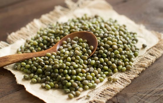 Uncooked Mung beans with a spoon on a wooden table
