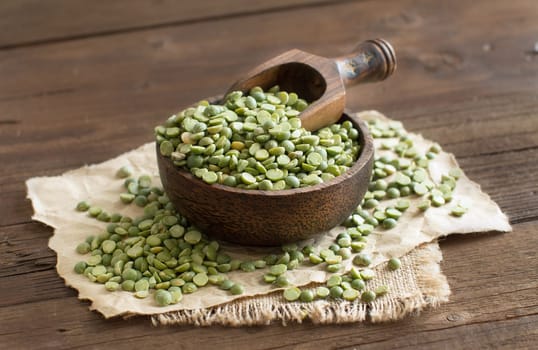 Uncooked Green Split Peas in a bowl with a spoon on a wooden table