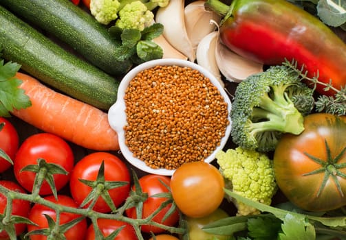 Uncookes brown millet in a bowl with vegetables top view