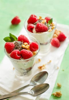 Yogurt with chia seeds, walnuts, mint and raspberries on green background