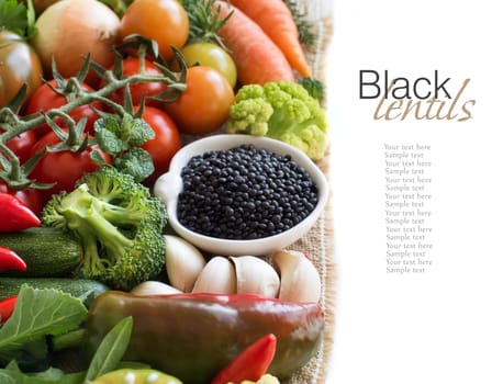 Uncooked black lentils in a bowl with vegetables isolated on white