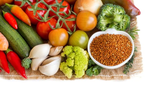 Uncooked brown millet in a bowl with vegetables isolated on white