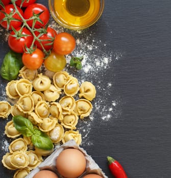 Fresh tortellini pasta and ingredients on a dark board top view