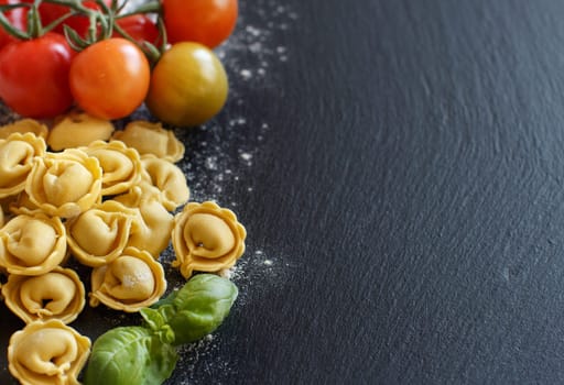 Fresh tortellini with basil ad tomatoes on a dark board top view